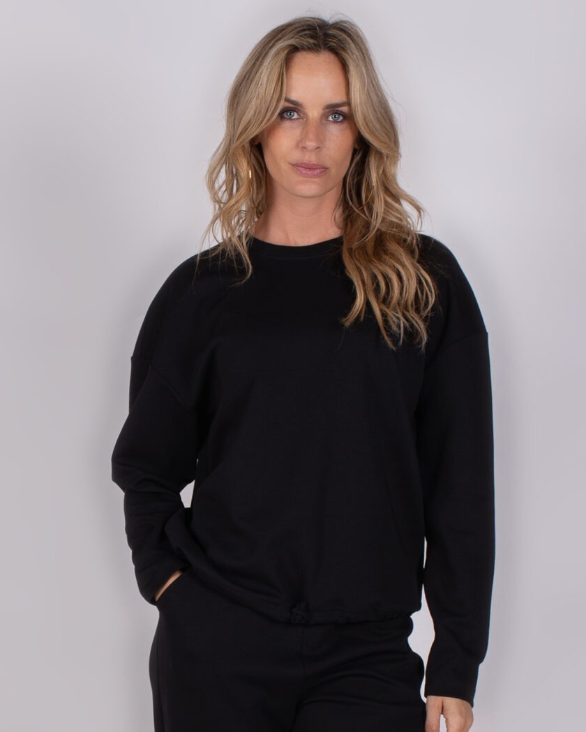 Vrouw in zwarte Studio_AW25-26-224 trui met lange mouwen en broek poseert voor een neutrale achtergrond.