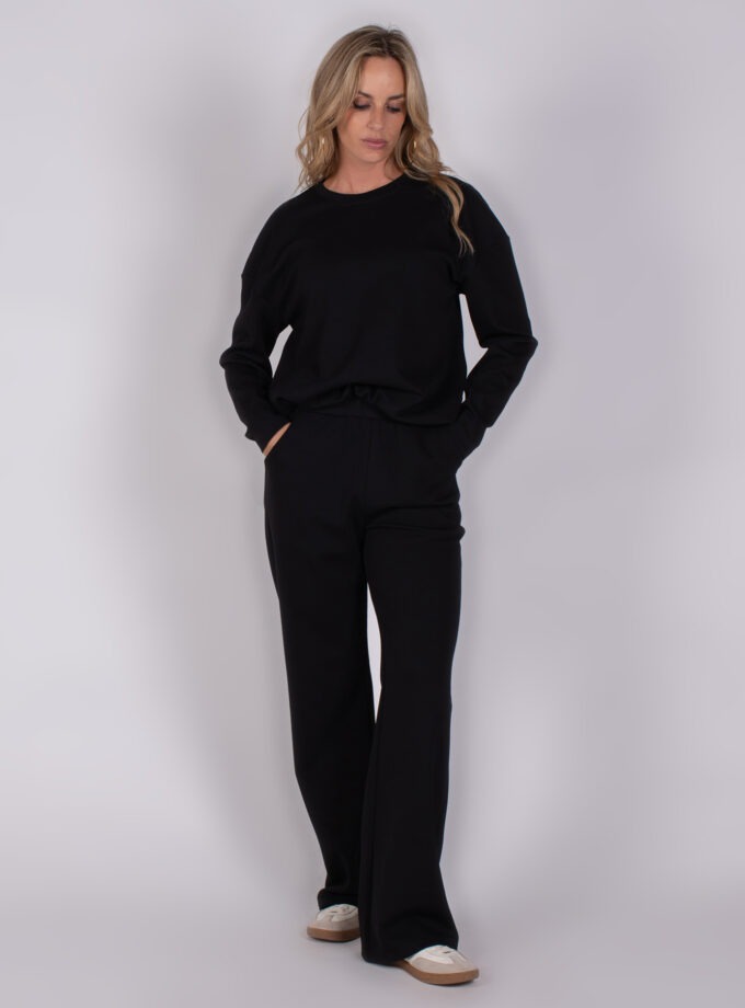 Vrouw draagt een zwarte comfortabele lounge-set met wijde broek en sneakers, model Studio_AW25-26-226.