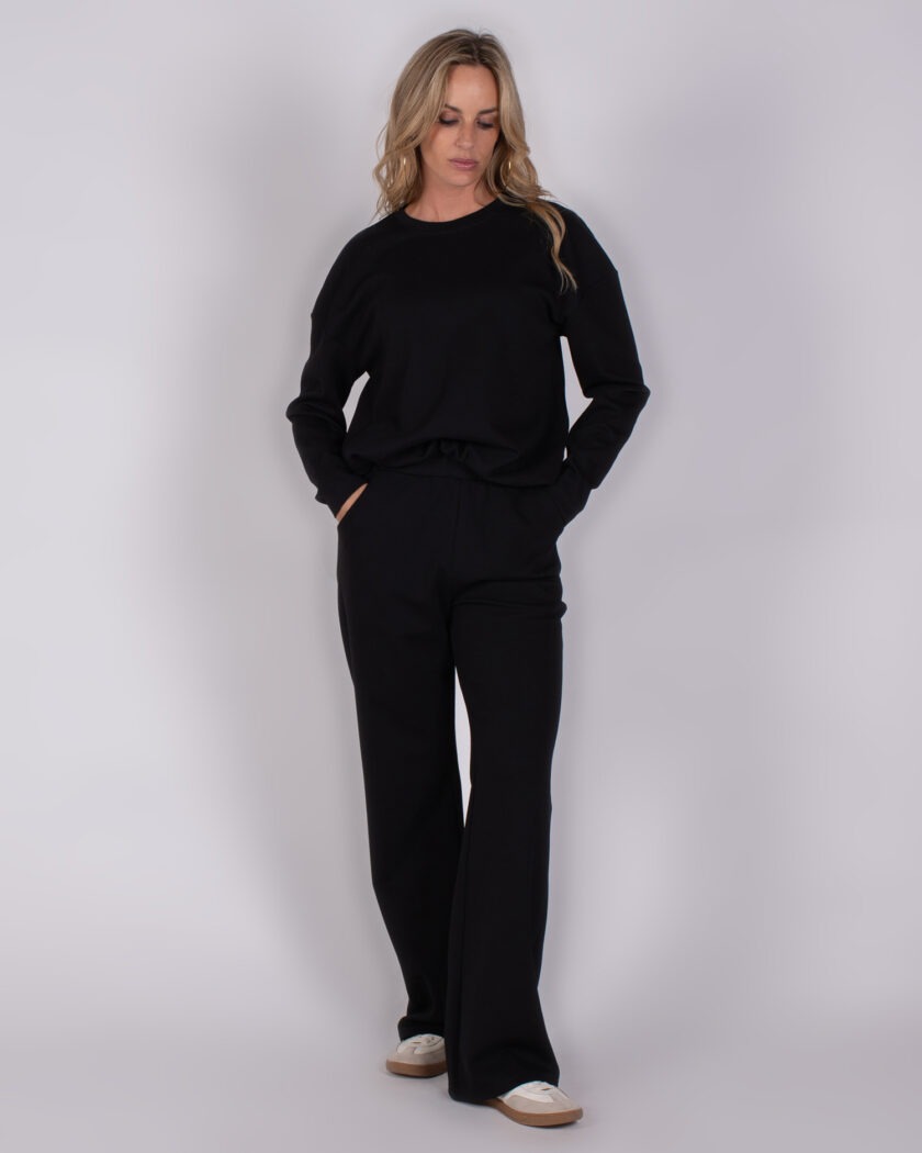 Vrouw draagt een zwarte comfortabele lounge-set met wijde broek en sneakers, model Studio_AW25-26-226.
