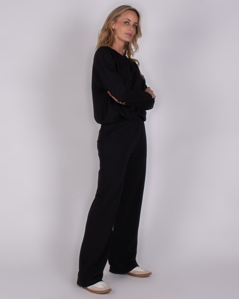 Vrouw draagt een zwarte lounge-set met lange mouwen en wijde broek uit de Studio AW25-26 collectie.