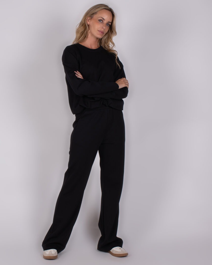 Vrouw draagt een zwarte, comfortabele loungetrenset uit de Studio AW25-26 collectie.