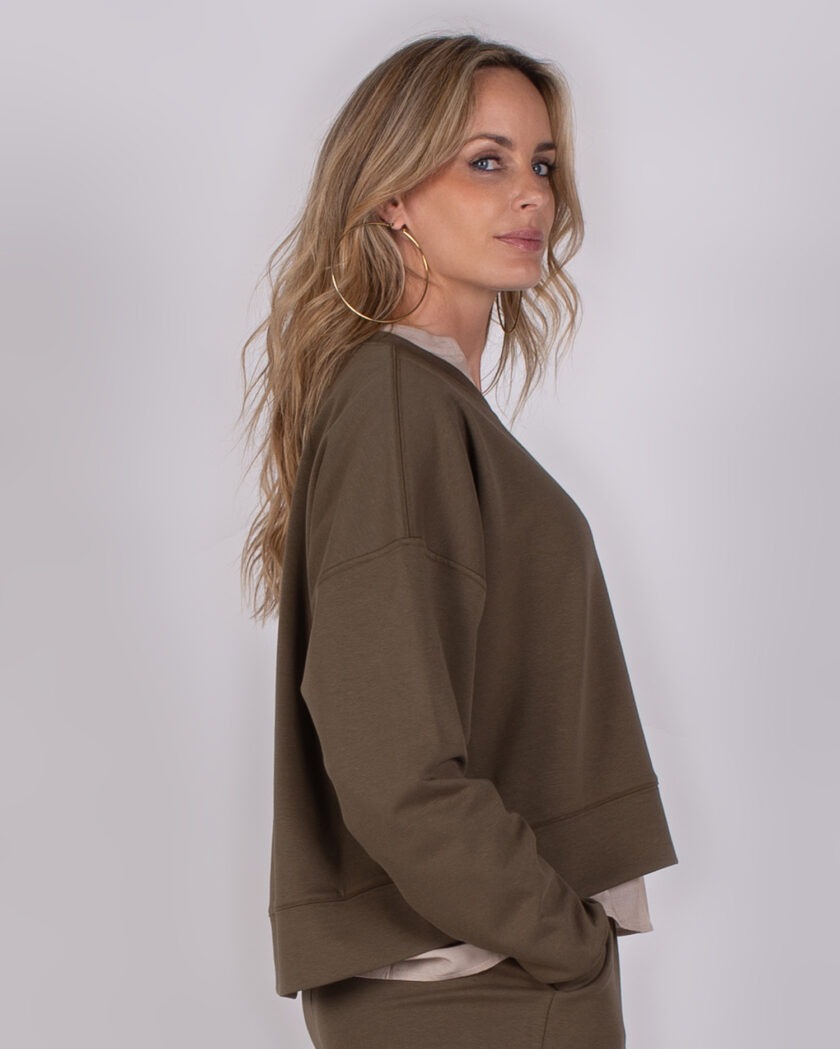 Vrouw in zijaanzicht draagt een olijfgroene trui met bijpassende broek uit de Studio AW25-26 collectie.