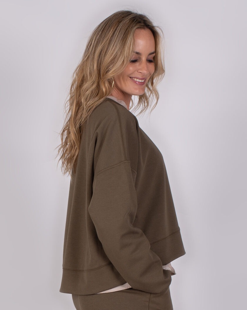 Vrouw in een olijfgroene Studio AW25-26-237 sweater en bijpassende broek, in zijaanzicht met een glimlach.
