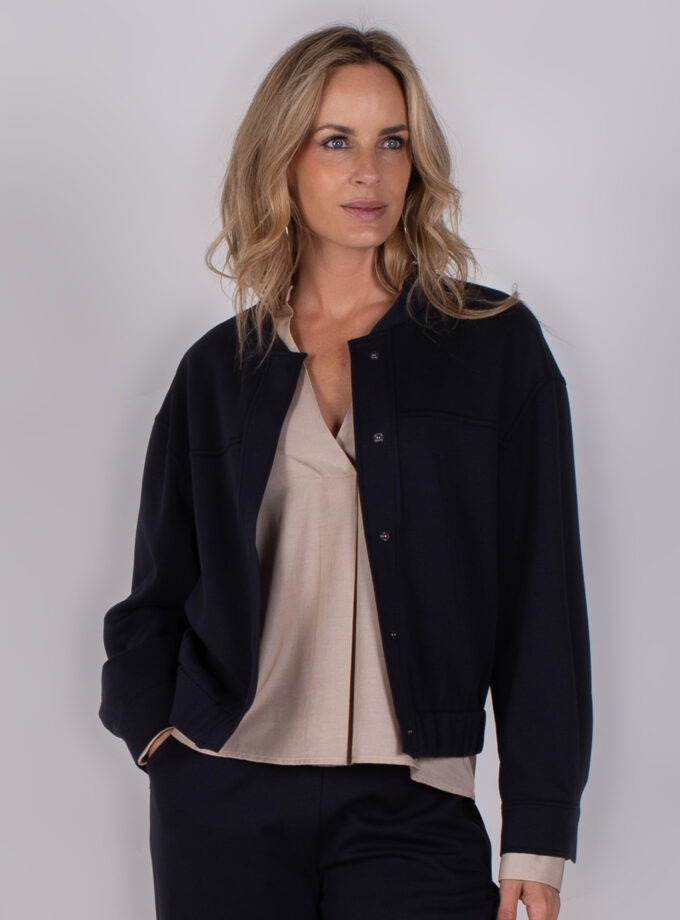 Vrouw draagt een donkerblauw jack over een beige blouse uit de Studio AW25-26-24 collectie.
