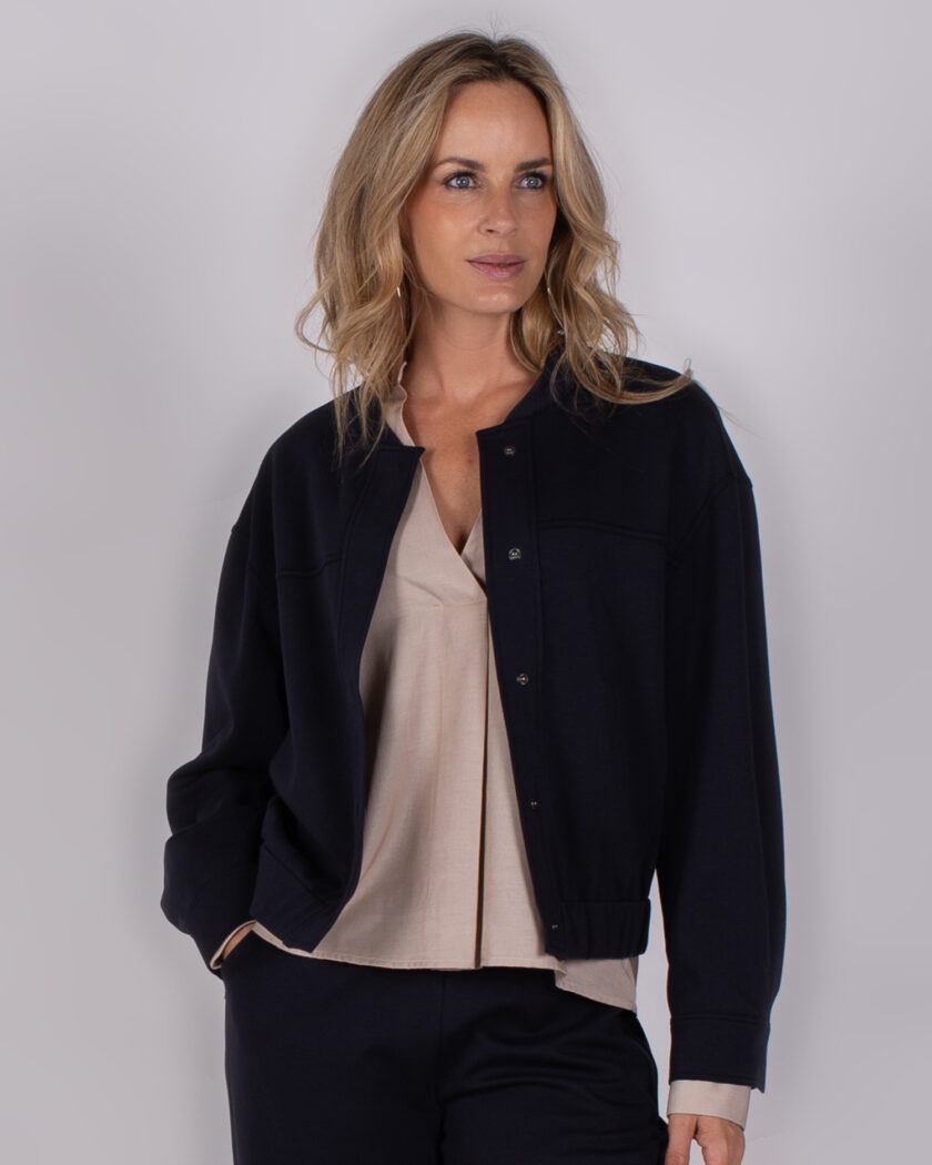Vrouw draagt een donkerblauw jack over een beige blouse uit de Studio AW25-26-24 collectie.
