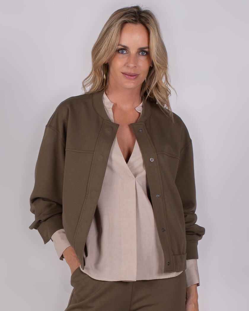 Vrouw draagt een olijfgroene bomberjack uit de Studio AW25-26 collectie over een beige blouse.