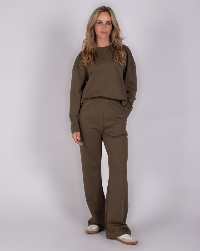 Vrouw draagt een olijfgroene lounge set bestaande uit een trui en wijde broek uit de Studio AW25-26 collectie.