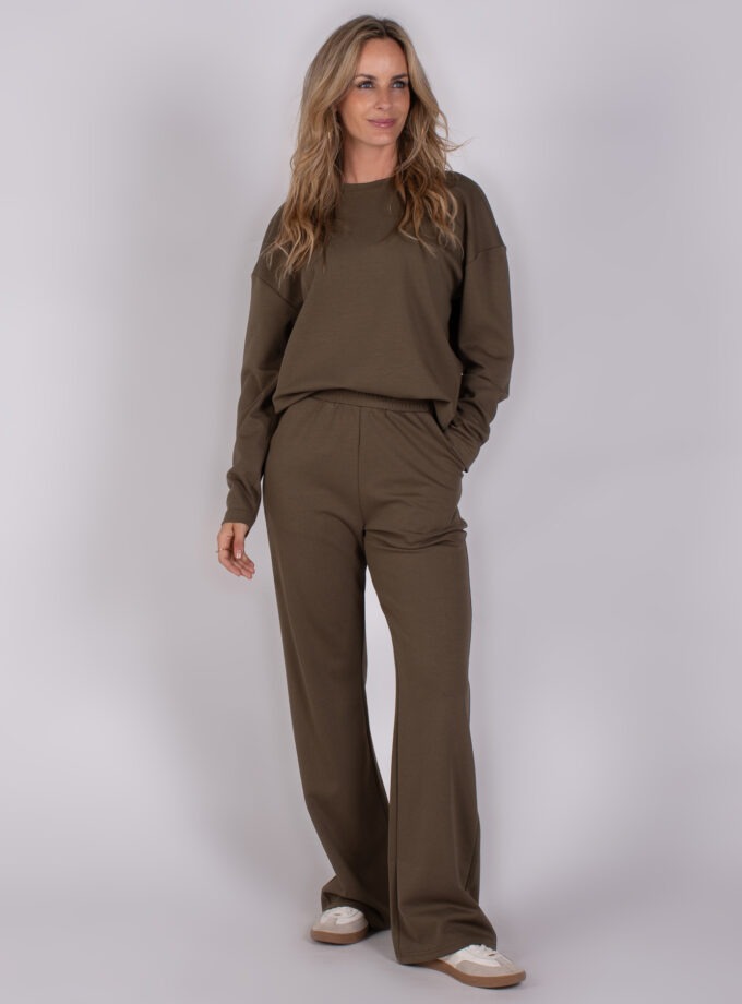 Vrouw in een comfortabele olijfgroene loungewear-set bestaande uit een sweater en wijde broek uit de Studio AW25-26 collectie.