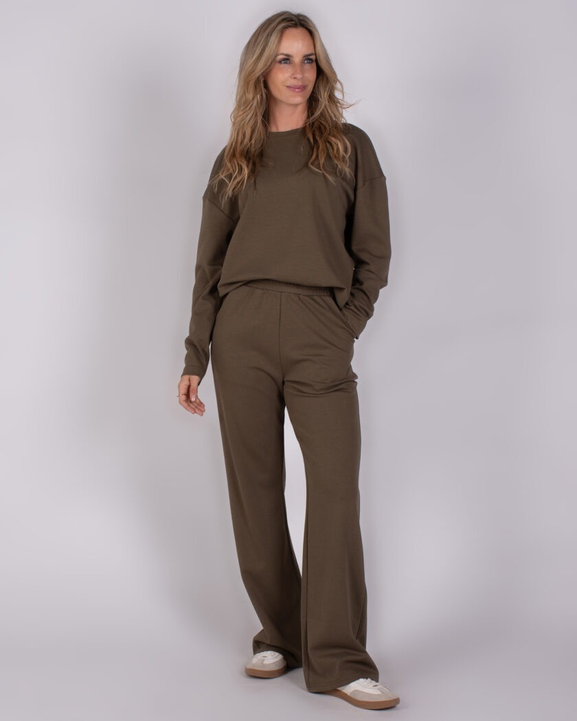 Vrouw in een comfortabele olijfgroene loungewear-set bestaande uit een sweater en wijde broek uit de Studio AW25-26 collectie.
