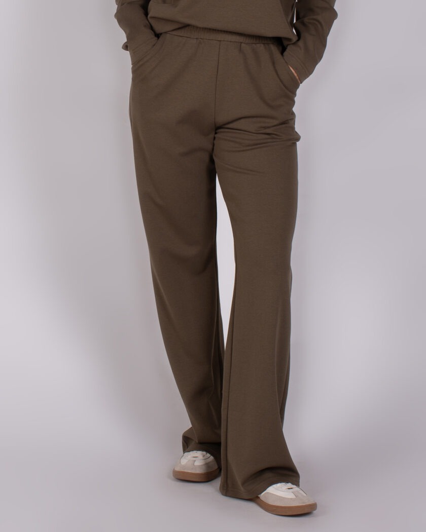 Model draagt een donkergroene, wijde Studio AW25-26-246 broek met elastische tailleband en witte sneakers.