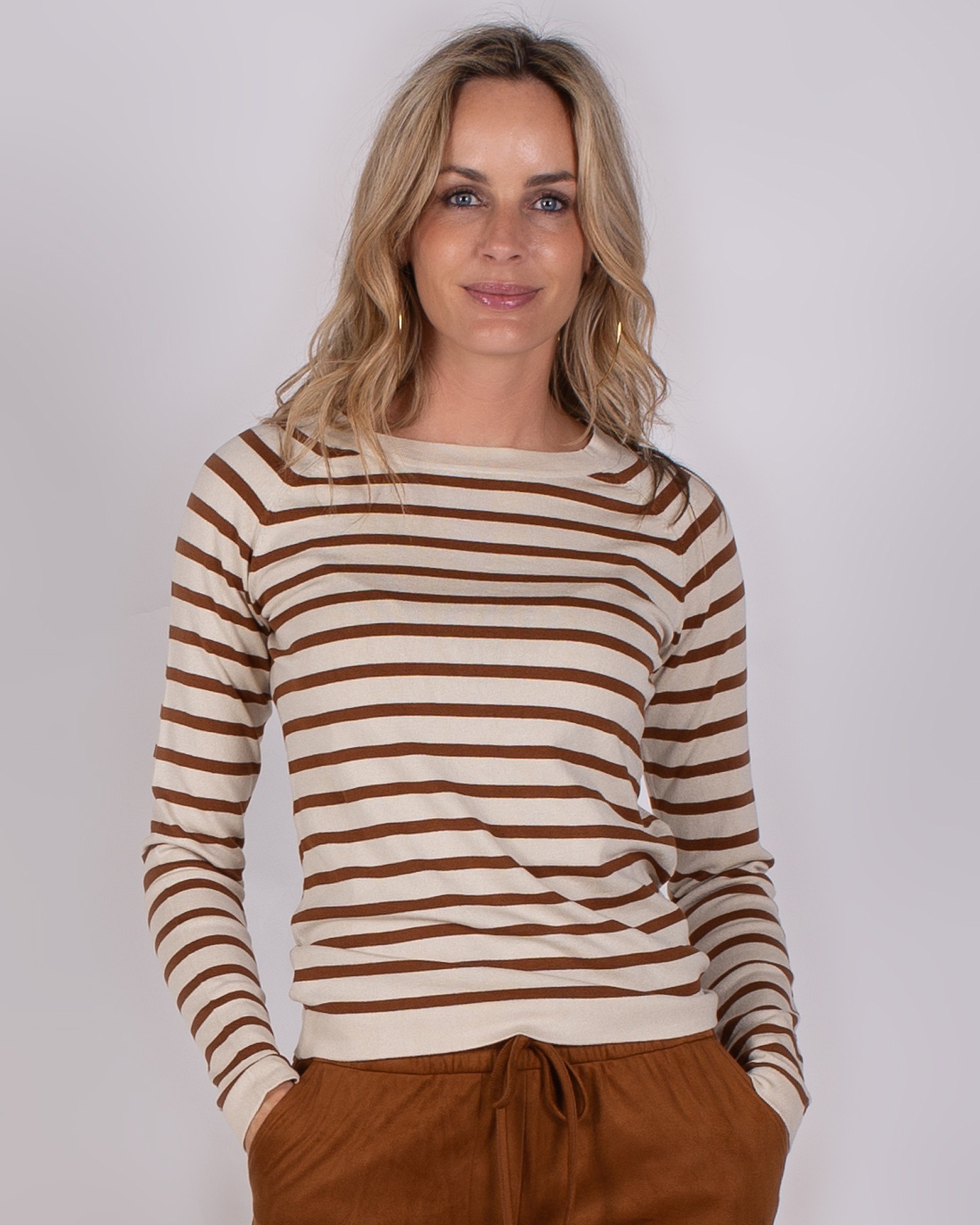 Vrouw met een beige en bruin gestreepte trui en bruine broek uit de Studio AW25-26 collectie.