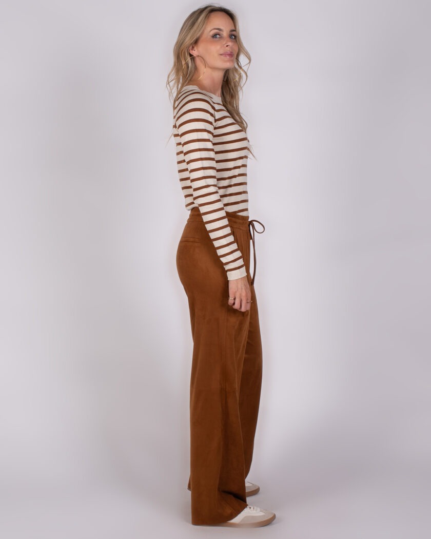 Vrouw in zijaanzicht draagt een beige-bruin gestreepte top en wijde, bruine broek van fluweelachtige stof uit de Studio AW25-26 collectie.
