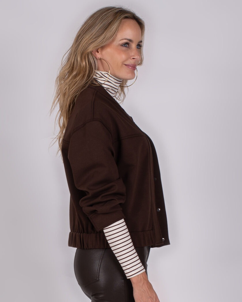 Vrouw in profiel met een donkerbruine jas uit de Studio AW25-26-278 collectie, gedragen over een gestreepte coltrui.