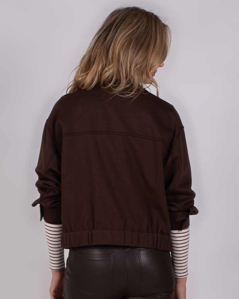 Achteraanzicht van een vrouw in een donkerbruine top met lange mouwen en een gestreepte top eronder, uit de Studio AW25-26 collectie.