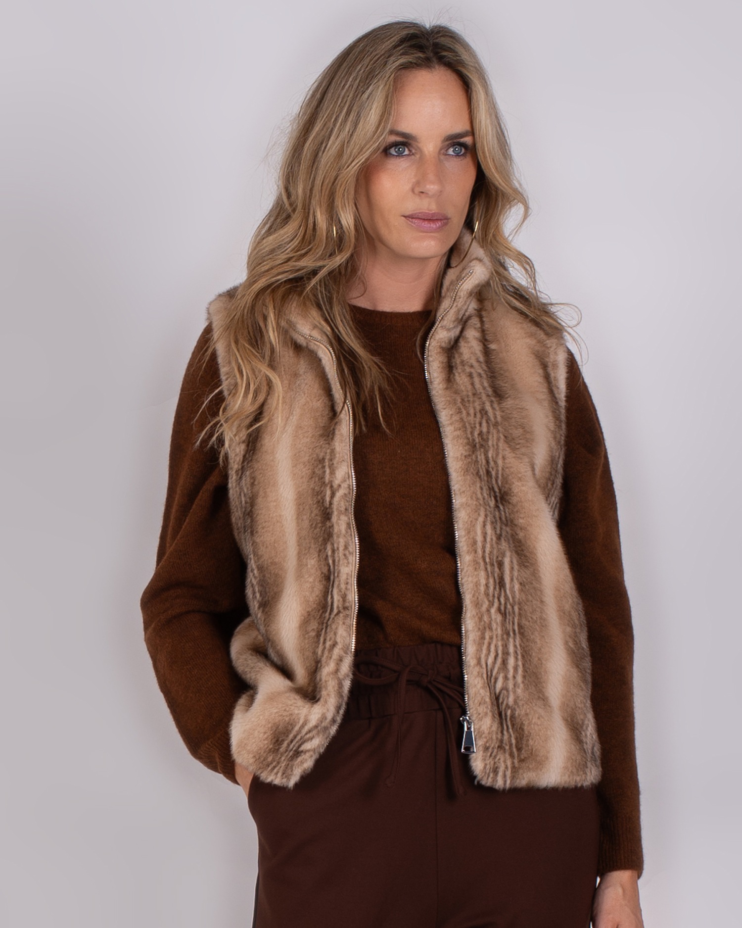 Vrouw draagt een bruine outfit met een zachte, lichtbruine bontlook bodywarmer uit de Studio AW25-26-28 collectie.