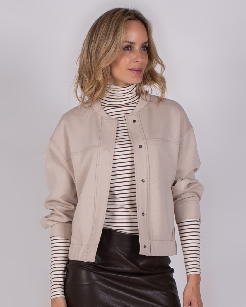 Model draagt een beige jack over een gestreepte coltrui en een zwarte leren rok uit de Studio AW25-26 collectie.