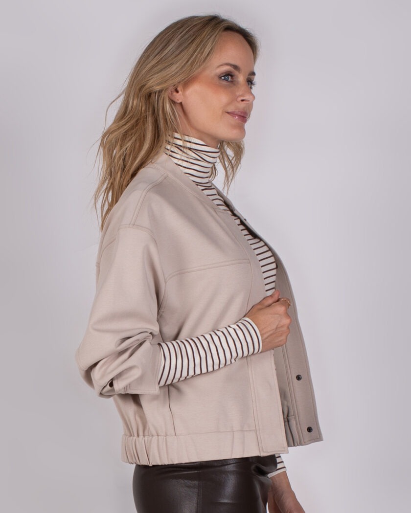 Vrouw in beige Studio AW25-26-286 jack met gestreepte coltrui en donkerbruine leren broek.