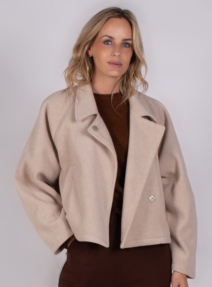 Vrouw draagt een beige oversized jas uit de Studio AW25-26-29 collectie over een donkerbruine top.