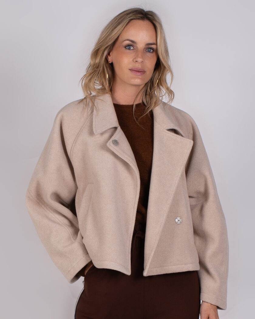 Vrouw draagt een beige oversized jas uit de Studio AW25-26-29 collectie over een donkerbruine top.
