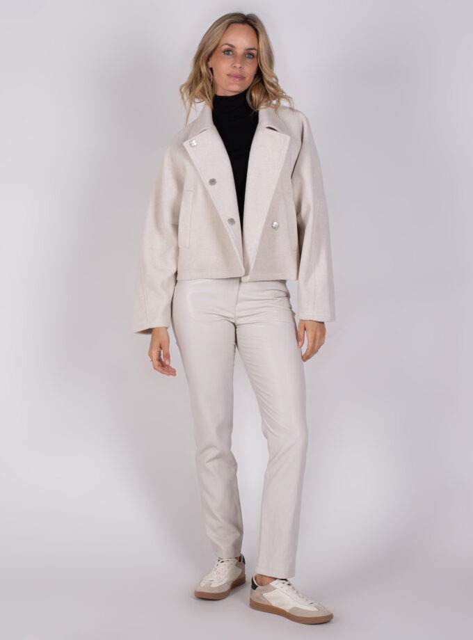 Vrouw draagt een stijlvolle Studio AW25-26-307 outfit met een lichtbeige jas, bijpassende broek en witte sneakers.