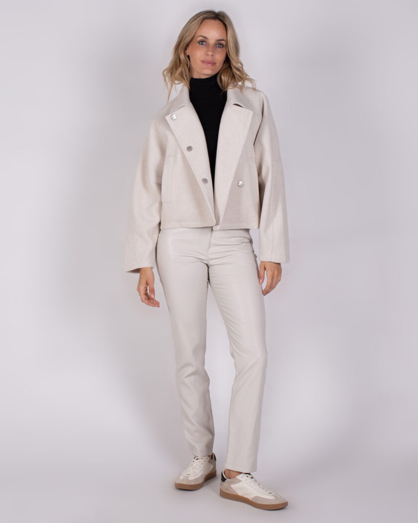 Vrouw draagt een stijlvolle Studio AW25-26-307 outfit met een lichtbeige jas, bijpassende broek en witte sneakers.