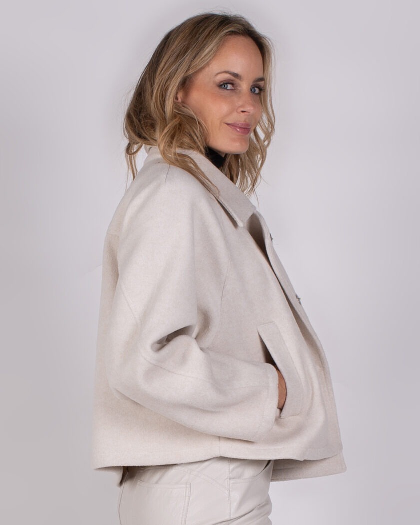 Vrouw draagt een lichtbeige cropped jas uit de Studio AW25-26-309 collectie en kijkt glimlachend over haar schouder.
