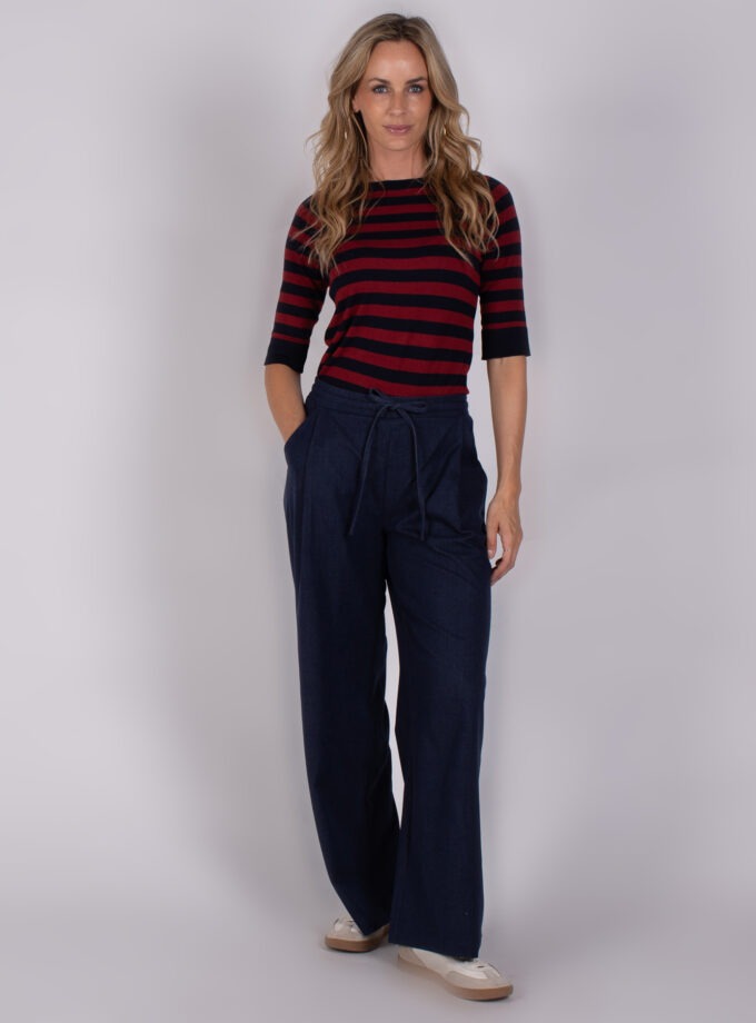 Vrouw in casual outfit met een rood-zwart gestreepte top en donkerblauwe wijde broek uit de Studio AW25-26-collectie.