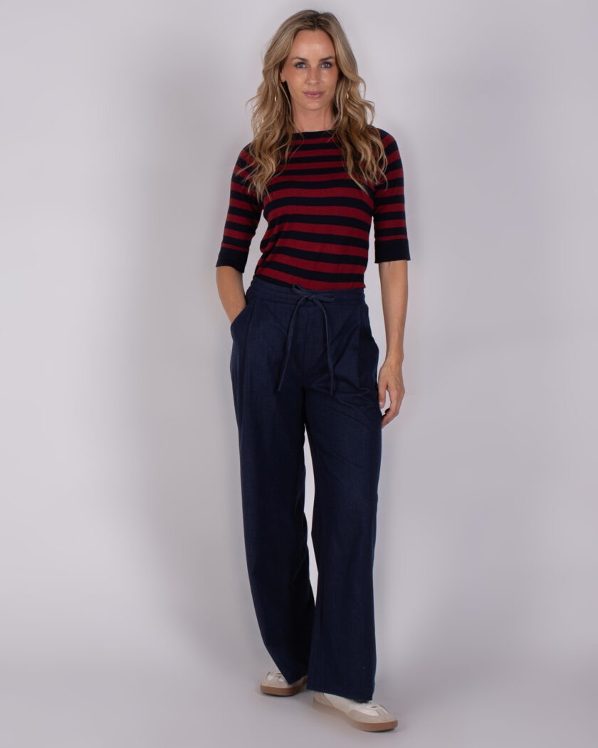 Vrouw in casual outfit met een rood-zwart gestreepte top en donkerblauwe wijde broek uit de Studio AW25-26-collectie.