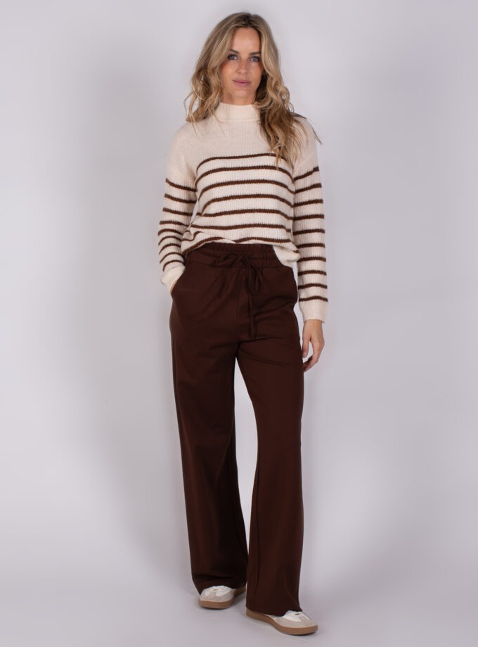 Vrouw draagt een crèmekleurige trui met bruine strepen en wijde, donkerbruine broek uit de Studio AW25-26 collectie.