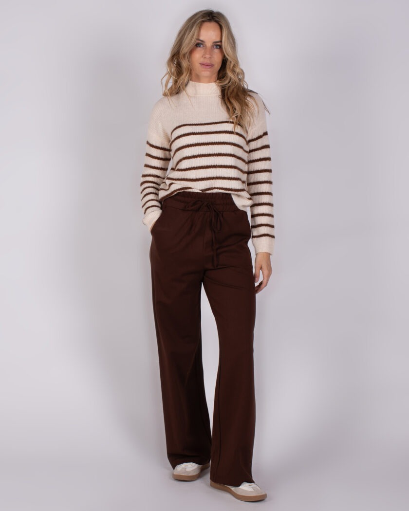 Vrouw draagt een crèmekleurige trui met bruine strepen en wijde, donkerbruine broek uit de Studio AW25-26 collectie.