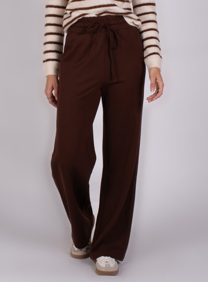 Vrouw in een gestreepte trui en wijde, donkerbruine broek met trekkoord uit de Studio AW25-26 collectie.