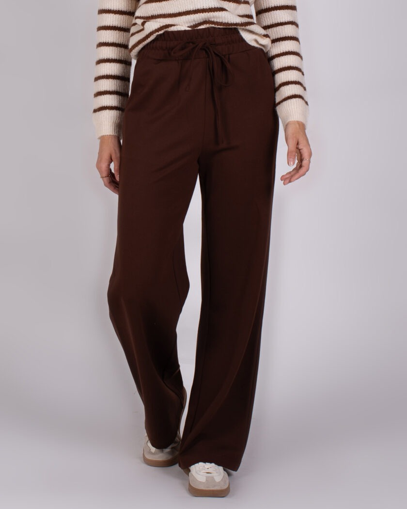 Vrouw in een gestreepte trui en wijde, donkerbruine broek met trekkoord uit de Studio AW25-26 collectie.