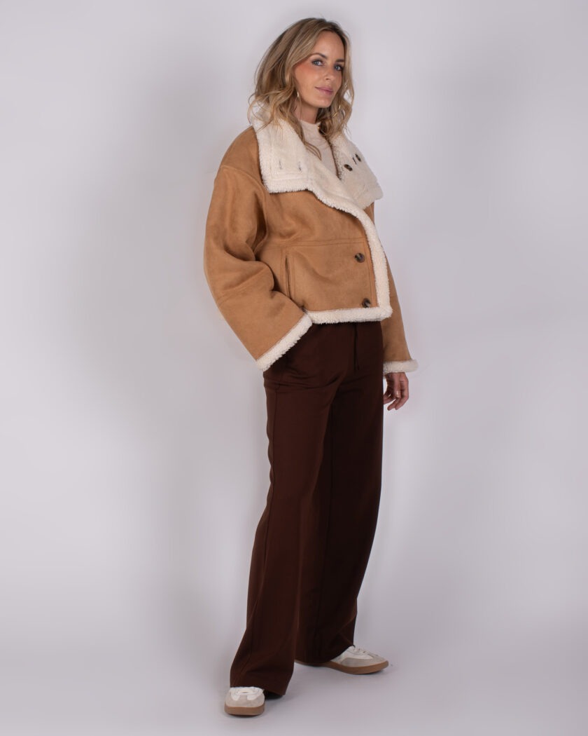 Vrouw draagt een beige shearling jas en donkerbruine broek uit de Studio AW25-26 collectie.