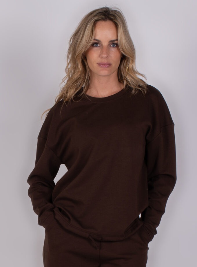 Vrouw poseert in een donkerbruine sweater en bijpassende broek uit de Studio AW25-26 collectie.