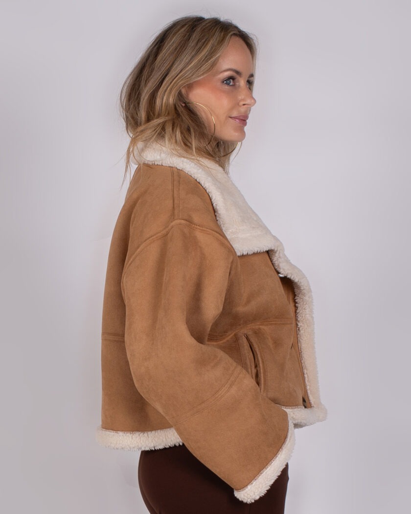Vrouw in profiel draagt een camel-kleurige shearling jas met witte voering uit de Studio AW25-26 collectie.