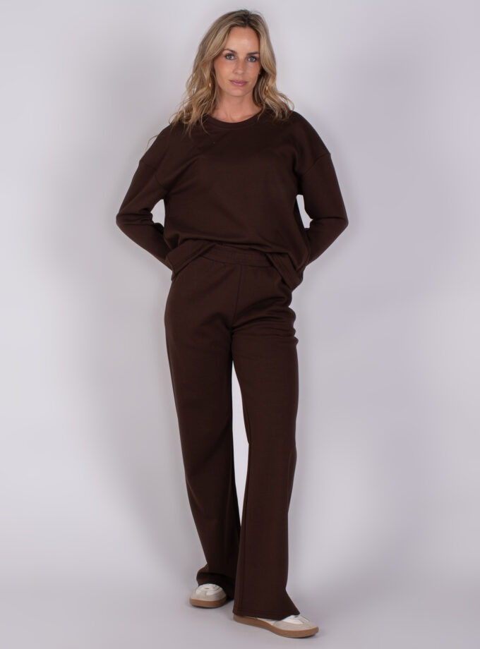 Vrouw draagt een donkerbruin, comfortabel loungewear-pak met lange mouwen en wijde broek.