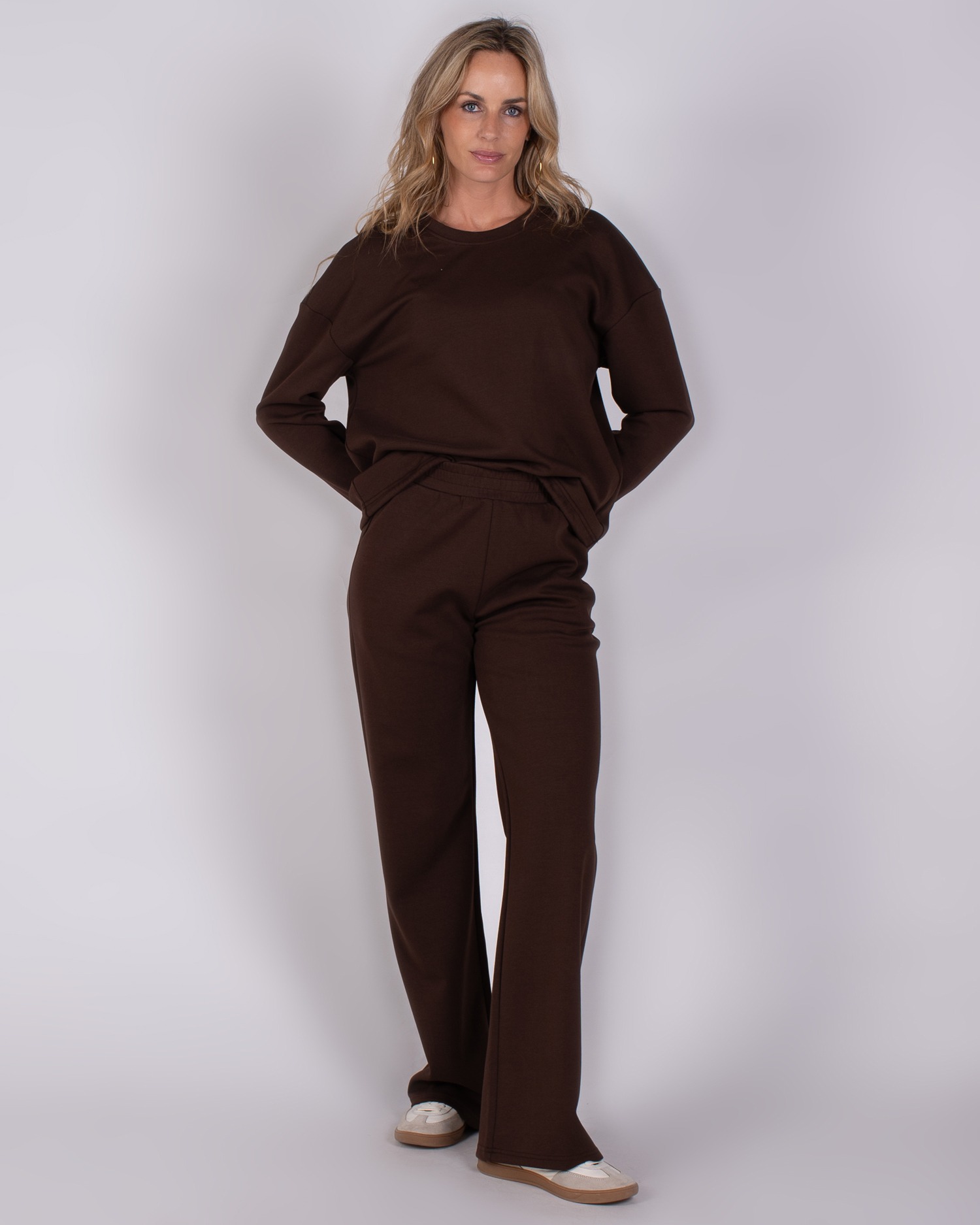 Vrouw draagt een donkerbruin, comfortabel loungewear-pak met lange mouwen en wijde broek.
