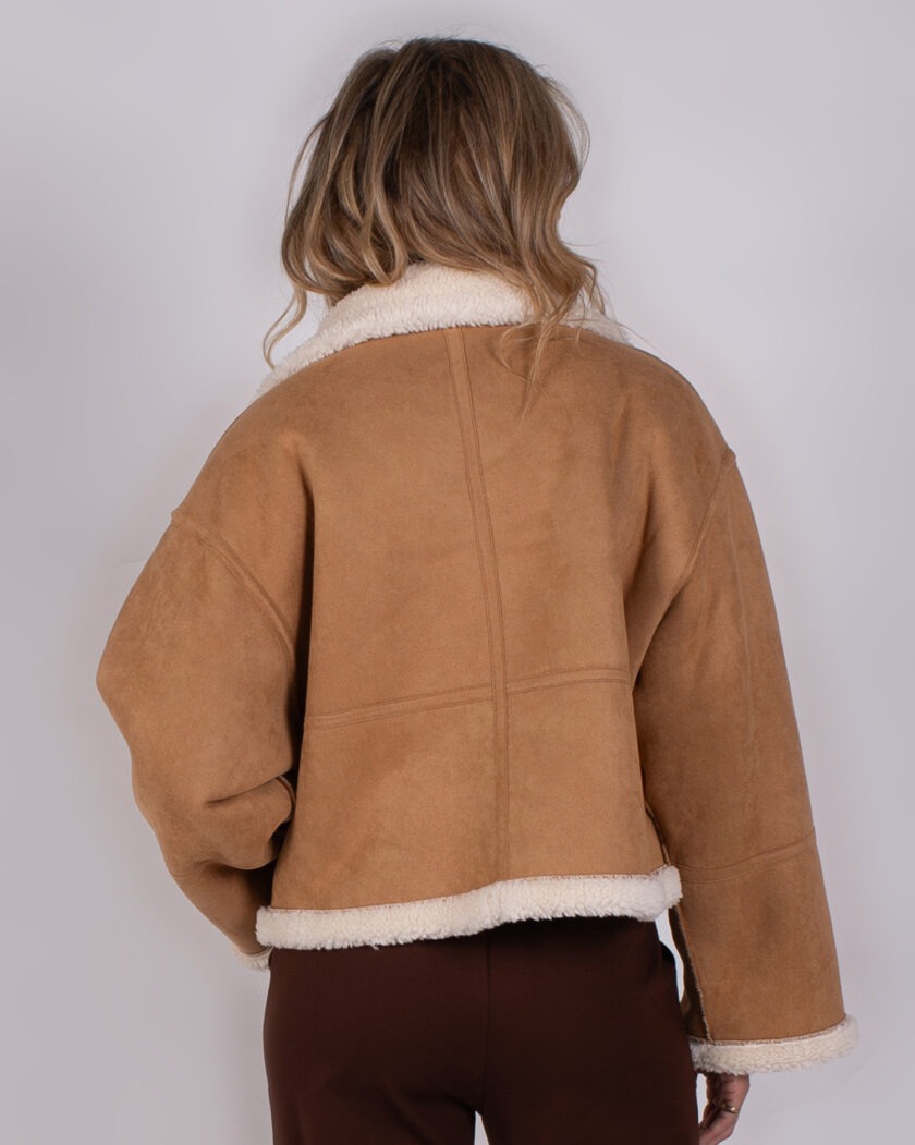 Achteraanzicht van een model dat een camel-kleurige shearling jas uit de Studio AW25-26 collectie draagt.