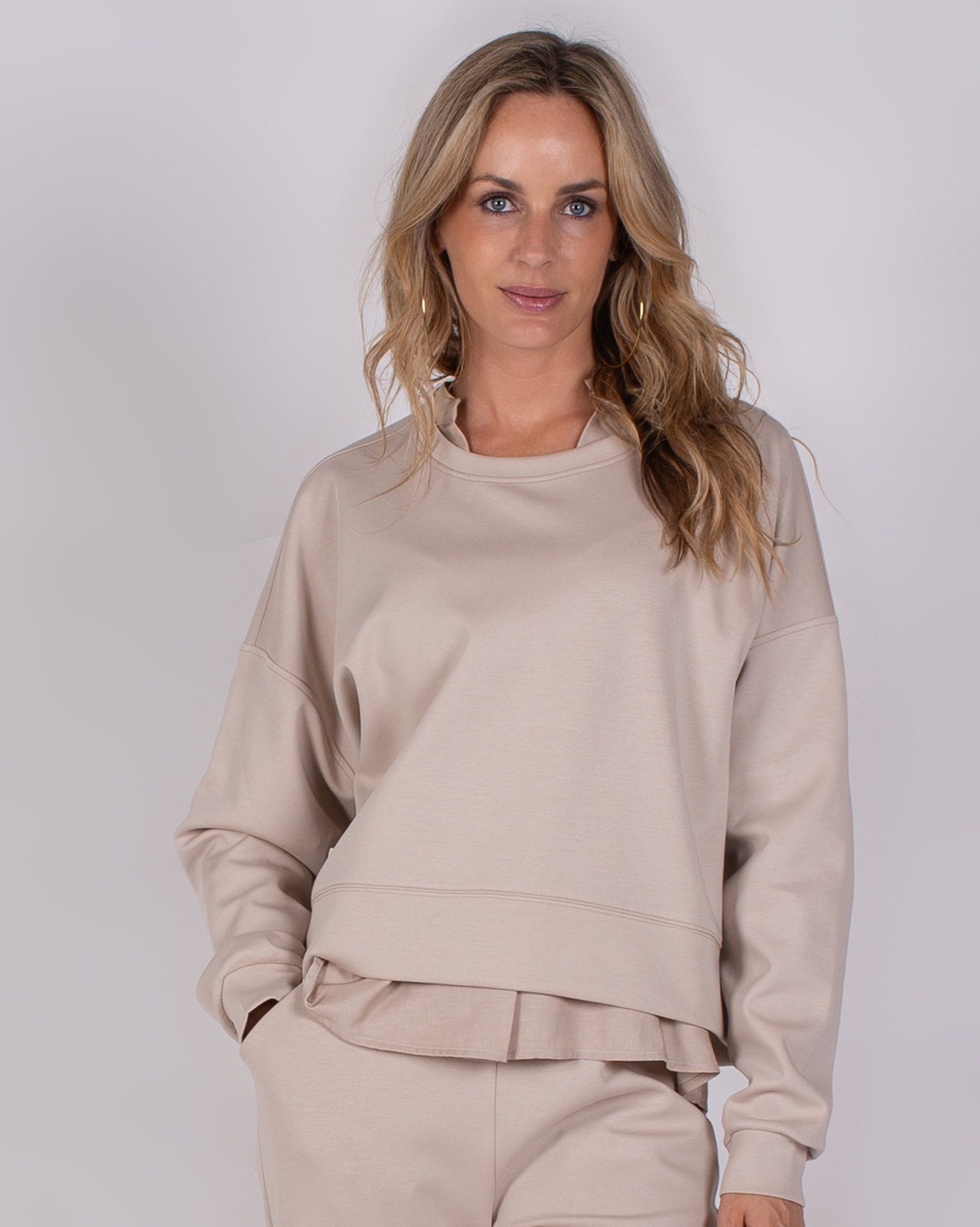 Vrouw draagt een beige loungepak uit de Studio AW25-26 collectie.
