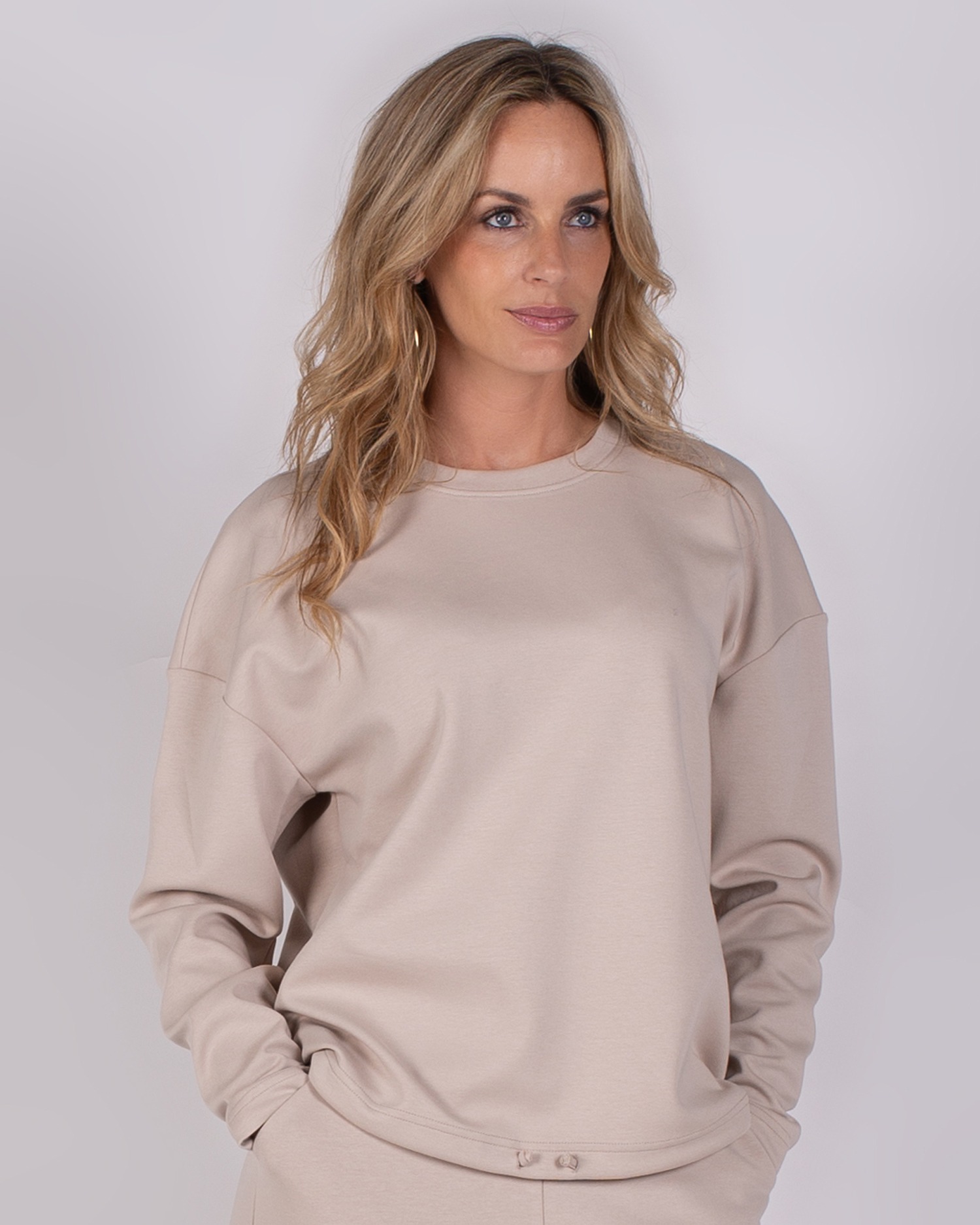 Vrouw draagt een beige trui uit de Studio AW25-26 collectie tegen een neutrale achtergrond.