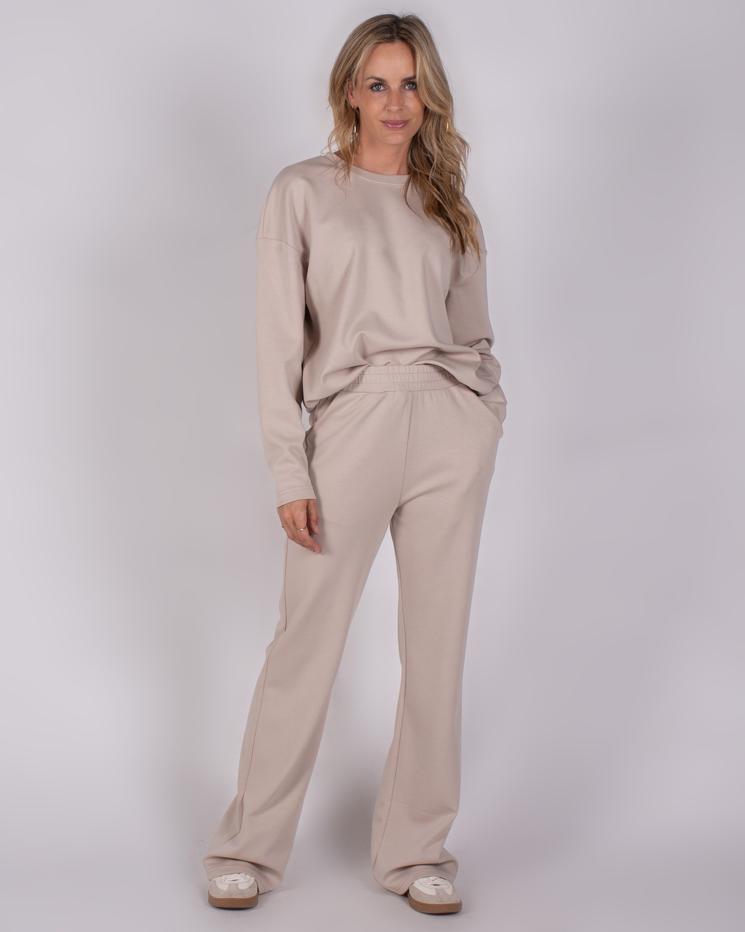 Vrouw draagt een beige loungewear-set bestaande uit een oversized trui en wijde broek uit de Studio AW25-26 collectie.