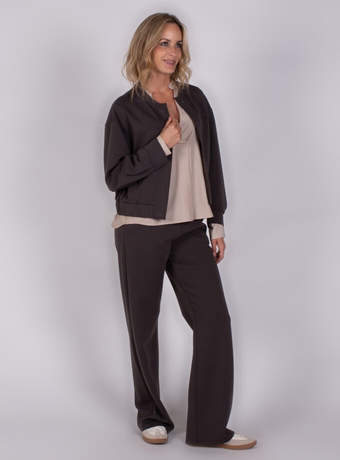 Vrouw poseert in een Studio AW25-26-46 outfit met een donkerbruin jasje, bijpassende broek en beige top.
