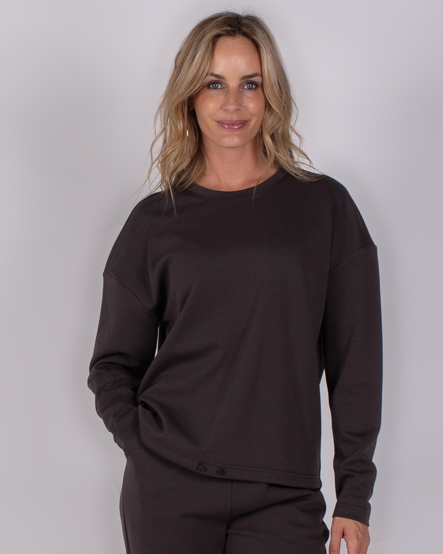 Vrouw draagt een donkerbruine lounge-outfit met lange mouwen uit de Studio AW25-26 collectie.