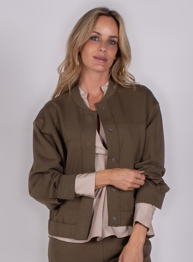 Vrouw draagt een olijfgroene jas met drukknopen uit de Studio AW25-26 collectie.