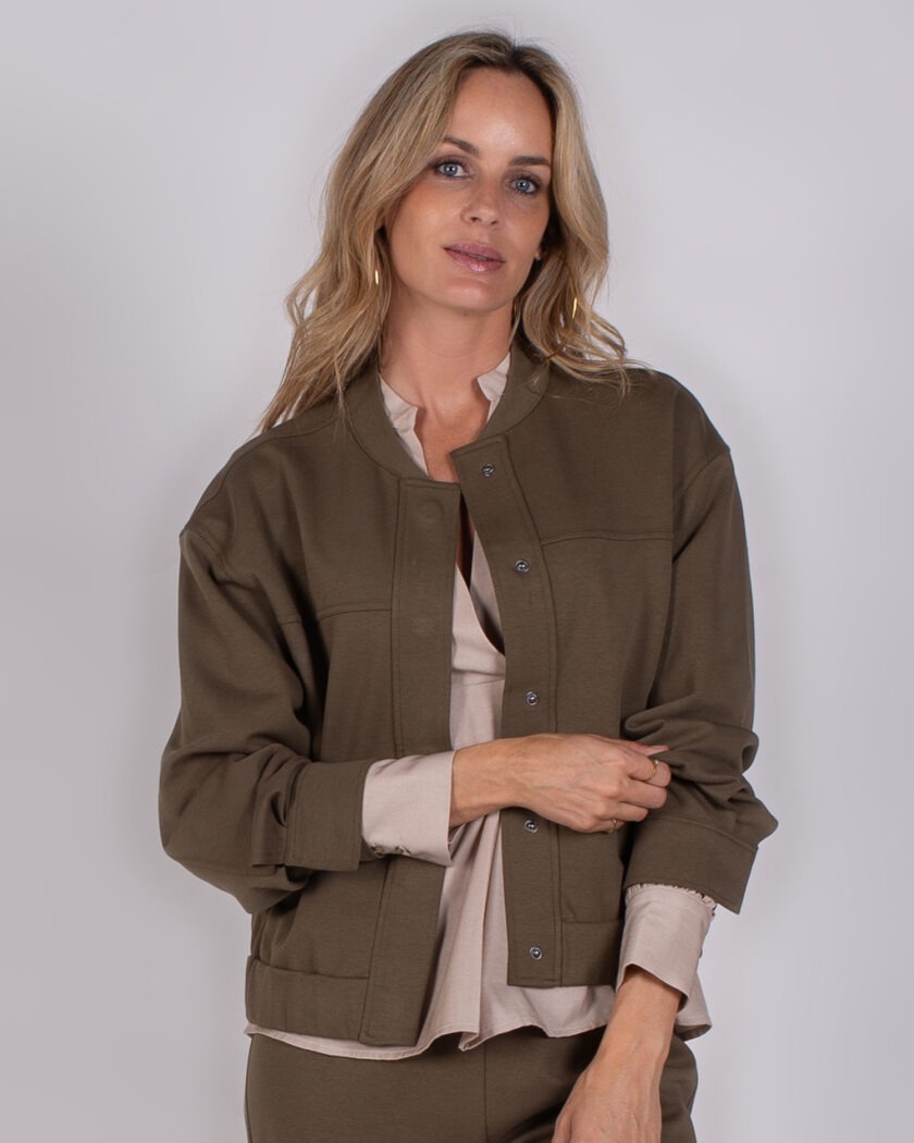Vrouw draagt een olijfgroene jas met drukknopen uit de Studio AW25-26 collectie.