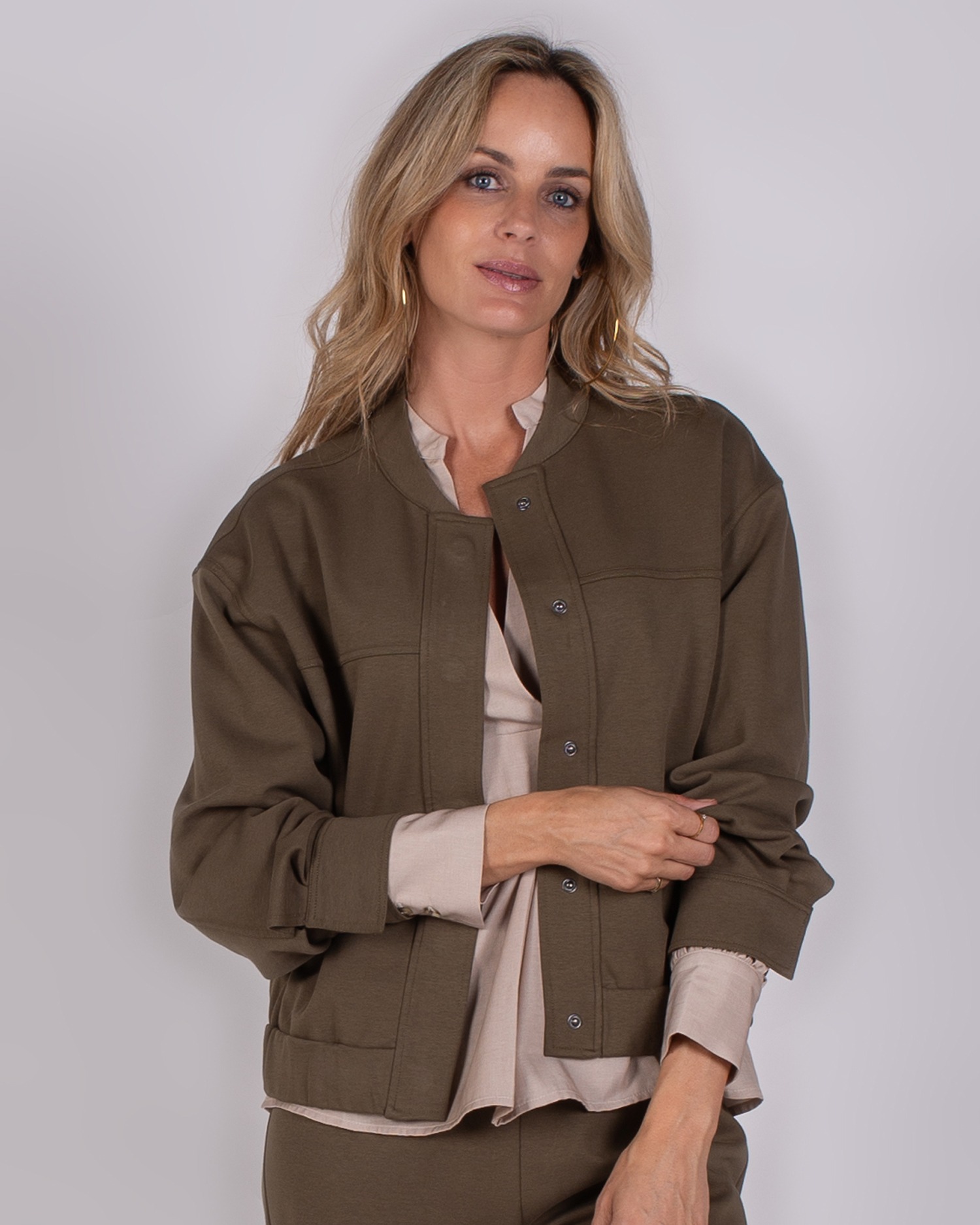 Vrouw draagt een olijfgroene jas met drukknopen uit de Studio AW25-26 collectie.