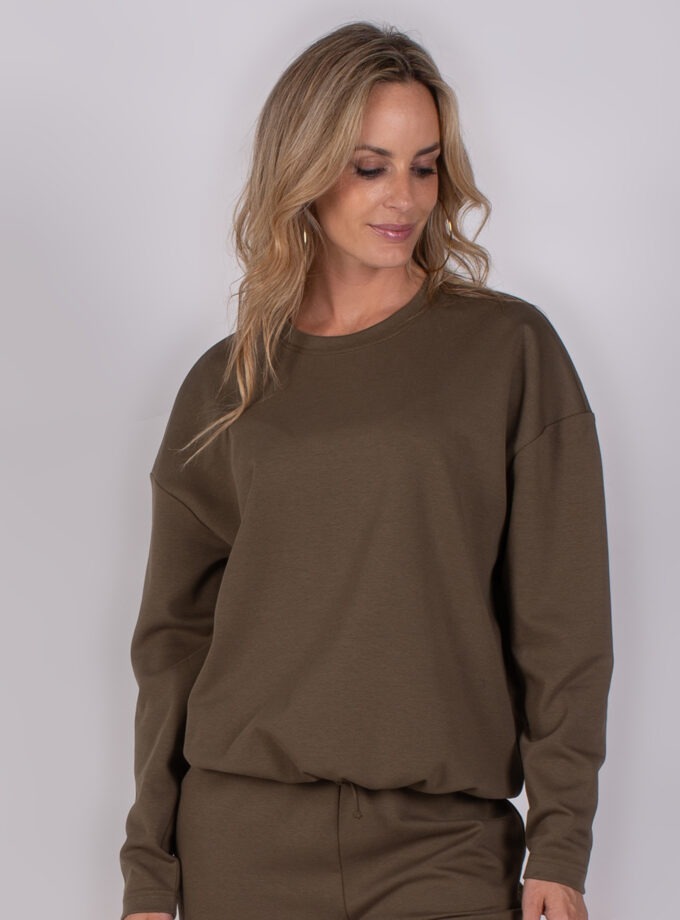 Vrouw draagt een donkerbruin loungepak met lange mouwen uit de Studio AW25-26 collectie.