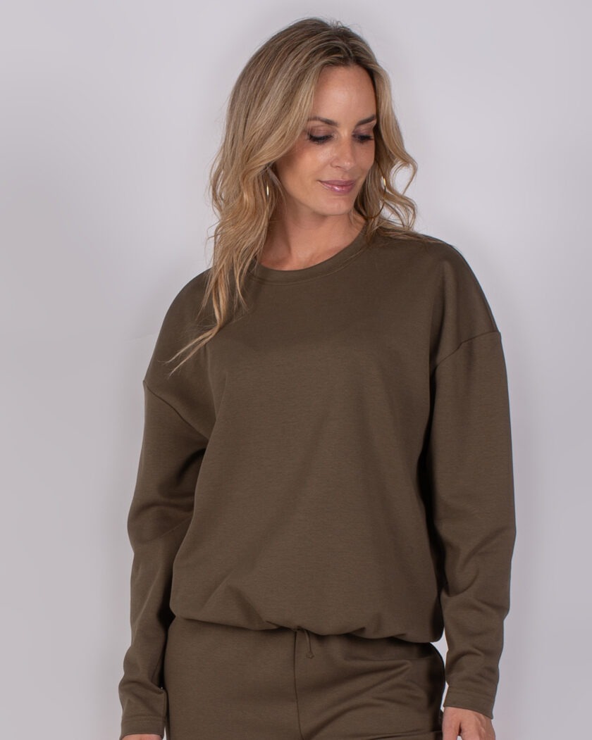 Vrouw draagt een donkerbruin loungepak met lange mouwen uit de Studio AW25-26 collectie.