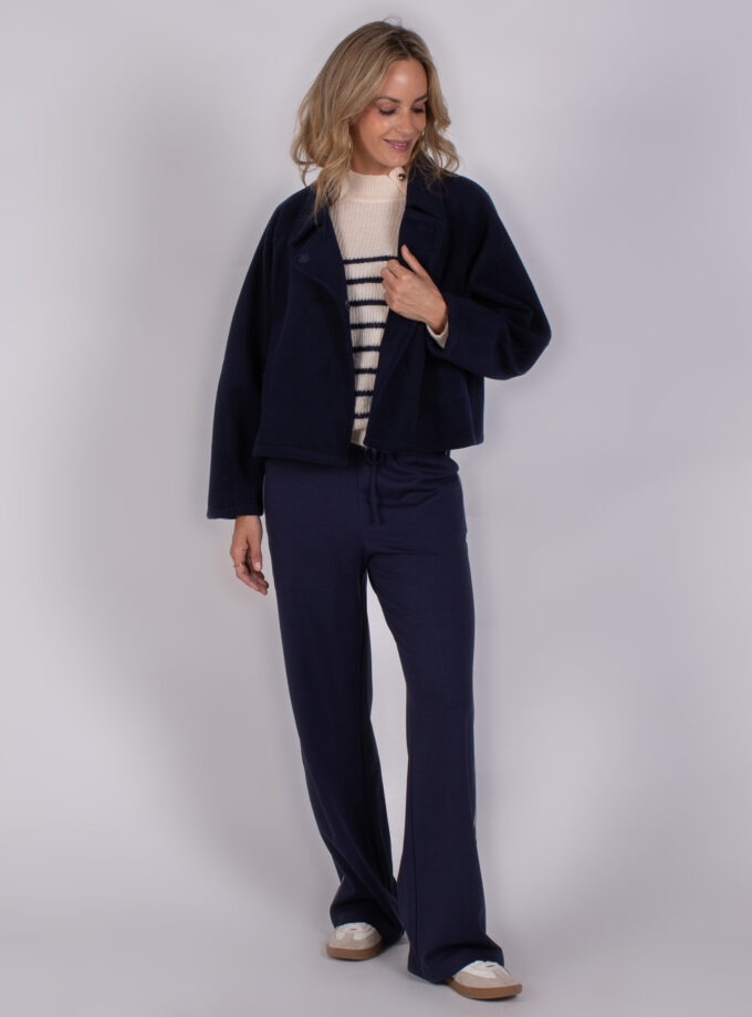 Vrouw in een Studio AW25-26-56 outfit met een donkerblauwe jas, gestreepte trui en donkerblauwe broek.