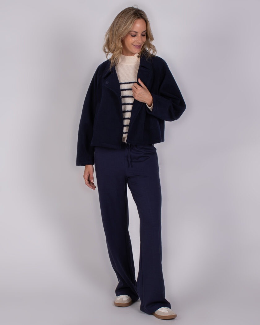 Vrouw in een Studio AW25-26-56 outfit met een donkerblauwe jas, gestreepte trui en donkerblauwe broek.